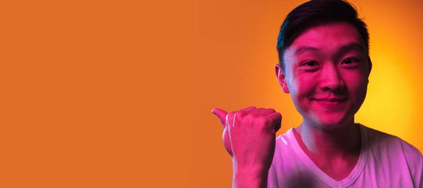Close-up Azji młody człowiek izolowane nad gradient pomarańczowy tło w świetle neonu. - Zdjęcie, obraz