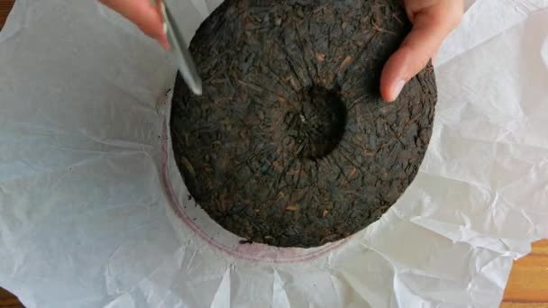 Shu Puerh cake chinese fermented black tea in white paper with knife. Male hands hold chip break pressed old round form ripened dark pu-erh into pieces. Healthy invigorating drinks coffee substitute. - Footage, Video