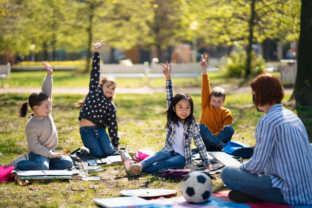 都会の公園で子供たちが屋外に座っている教師、学習グループ教育の概念. - 写真・画像