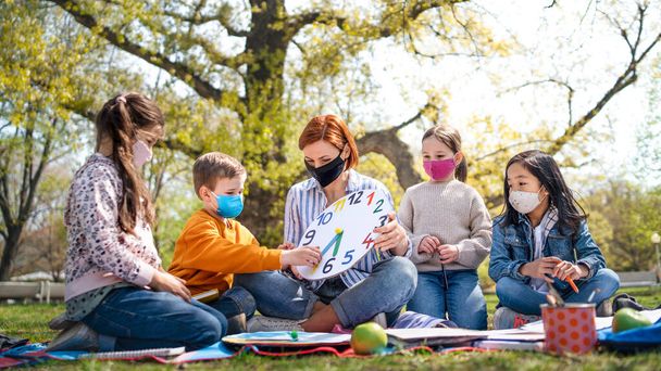 Teacher with small children sitting outdoors in city park, learning group education and coronavirus concept. - Φωτογραφία, εικόνα