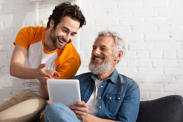 Smiling man pointing at digital tablet near mature father at home  - Fotoğraf, Görsel
