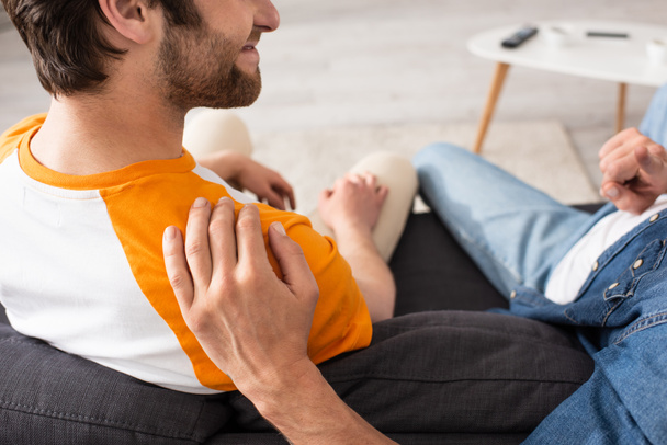 Cropped view of man hugging and pointing with finger near smiling son on couch  - Fotoğraf, Görsel
