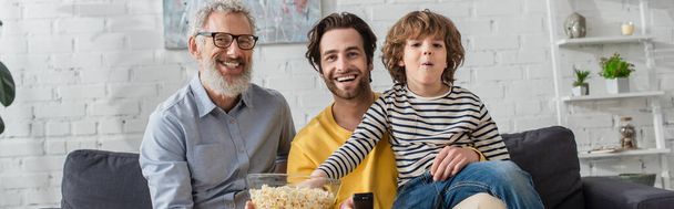Smiling man holding popcorn near son and kid during movie, banner  - 写真・画像