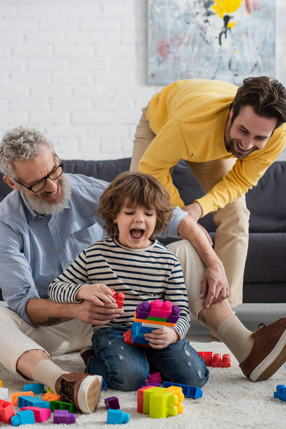 Cheerful parents playing building blocks with boy on carpet  - Fotoğraf, Görsel