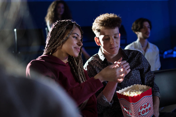 Young couple eating popcorn while watching movie in cinema. - Φωτογραφία, εικόνα
