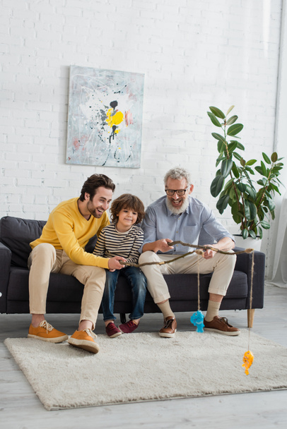 Smiling men and kid playing fishing in living room  - Photo, Image