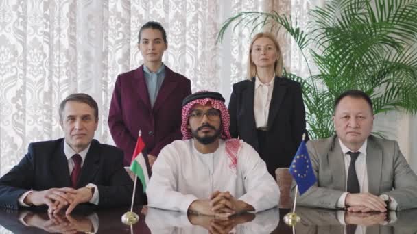 Střední pomalý portrét tří ministrů zahraničních věcí středního věku z různých zemí a jejich asistentek při pohledu do kamery na jednacím stole v moderní konferenční místnosti - Záběry, video