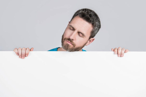 hombre barbudo dormido cansado detrás de la pancarta de papel blanco en blanco con espacio de copia para el anuncio, recomiendan. - Foto, Imagen