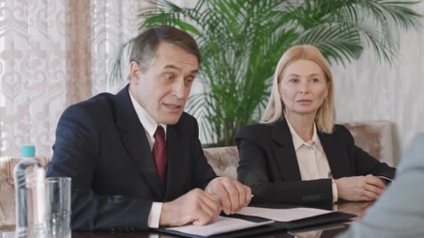 Талия PAN-шот кавказской пары инвесторов среднего возраста, беседующих со своими деловыми партнерами, обсуждающих новый проект в ярком современном конференц-зале - Кадры, видео