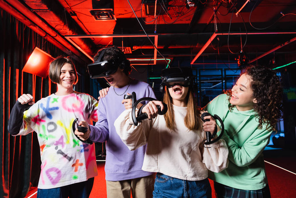 happy boy showing win gesture near interracial teenagers in vr game zone - Photo, Image