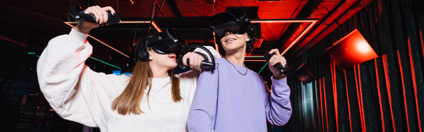 счастливые подростки-геймеры в наушниках развлекаются в игровой зоне VR, баннер - Фото, изображение
