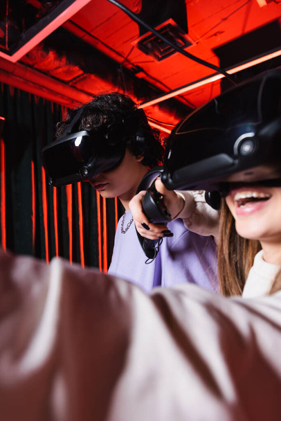 cheerful girl gaming in vr headset near teenage boy, blurred foreground - Photo, Image