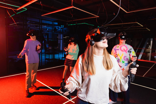 astonished teenage girl gaming in vr headset near multiethnic friends - Photo, Image