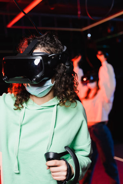 interracial girls in medical masks and vr headsets gaming in play zone on blurred background - Photo, Image