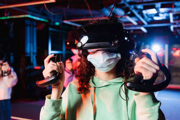 african american girl in medical mask and vr headset gaming near blurred friends - 写真・画像