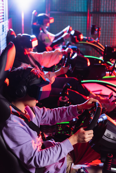 adolescentes en auriculares vr carreras en simuladores de coche sobre fondo borroso - Foto, Imagen