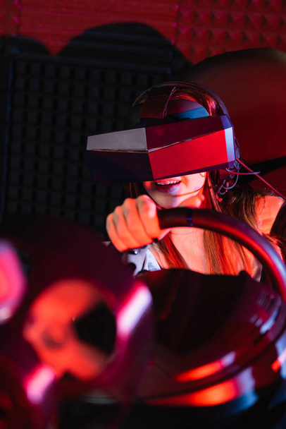 smiling girl in vr headset racing in car simulator on blurred foreground - Foto, Bild