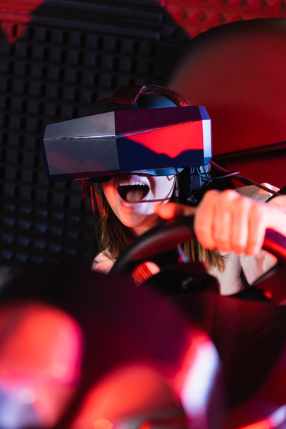 astonished girl playing racing game in car simulator, blurred foreground - Фото, зображення
