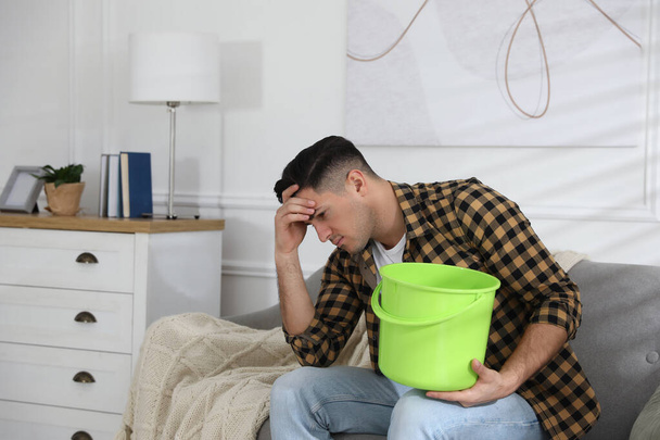Эмоциональный человек собирает воду, протекающую с потолка в гостиной. Поврежденная крыша - Фото, изображение
