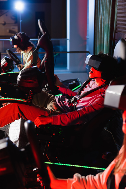 užaslý hráč závodní na auto simulátor v blízkosti rozmazané přátele - Fotografie, Obrázek