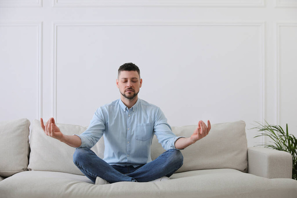 Man meditating on comfortable sofa in living room - Foto, imagen
