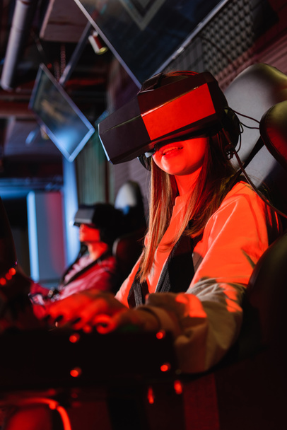 smiling girl in vr headset gaming on car racing simulator, blurred foreground - Zdjęcie, obraz
