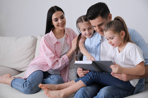Father reading book to family on sofa in living room - Φωτογραφία, εικόνα