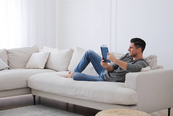 Man with book lying on comfortable sofa in living room - Foto, Imagem