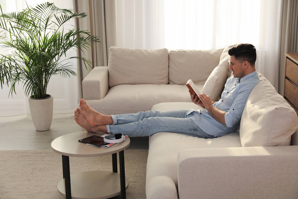 Man reading book on sofa in living room - Фото, изображение