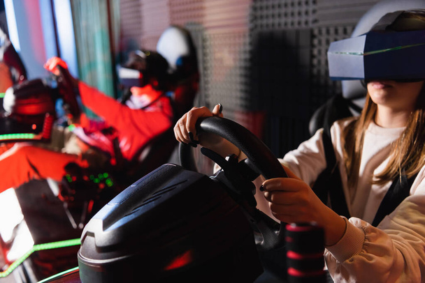 vrienden in vr headsets spelen racespel op auto simulatoren, wazig voorgrond - Foto, afbeelding