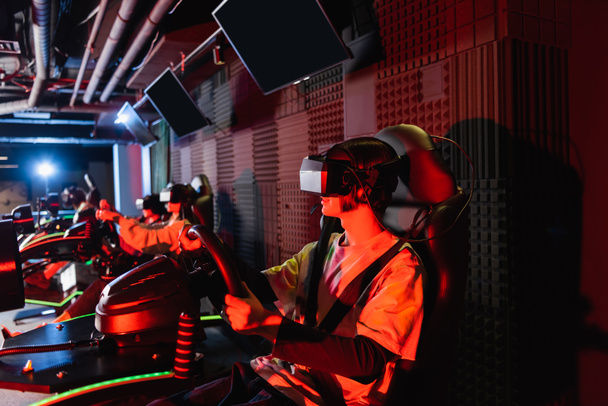 teenage gamers in vr headsets racing on car simulators in play zone - Photo, Image