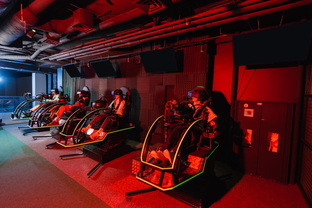 teenage friends in virtual reality headsets gaming on racing simulators - Photo, Image