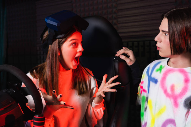 astonished girl gesturing while talking to friend near car simulator - Zdjęcie, obraz