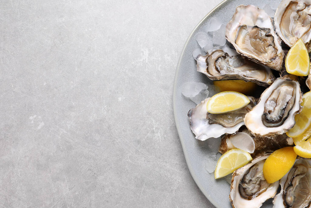 Fresh oysters with lemon and ice on grey table, top view. Space for text - 写真・画像
