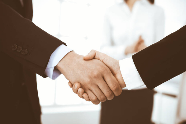 Businessman and woman shaking hands with colleagues at the background. Handshake at meeting in office. Concept of success in business - Foto, Bild