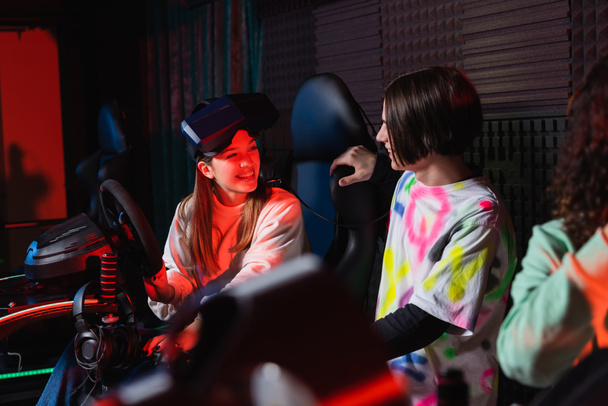adolescente hablando con chica sonriente en simulador de carreras de coches - Foto, imagen