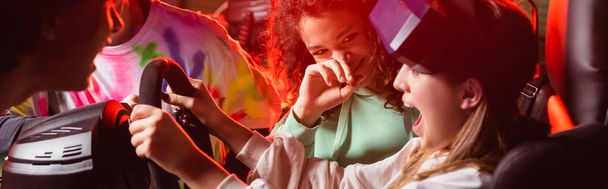 adolescentes multiétnicos rindo perto de menina assustada no simulador de carro, banner - Foto, Imagem
