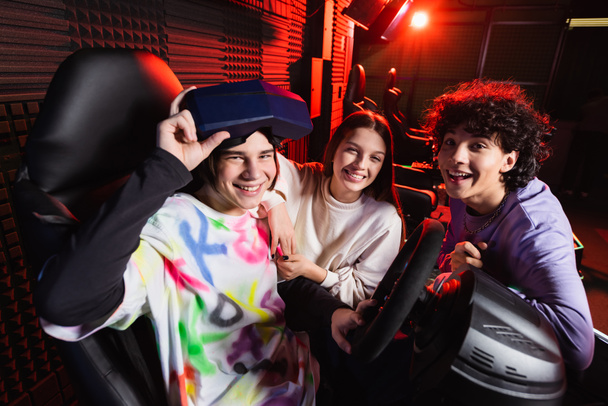 giocatori felici sorridenti alla fotocamera vicino al simulatore di corse automobilistiche - Foto, immagini