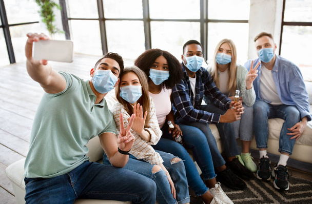 Група багатоетнічних друзів в масках, які беруть селфі зі смартфоном на соціальні збори вдома, носячи захист
 - Фото, зображення