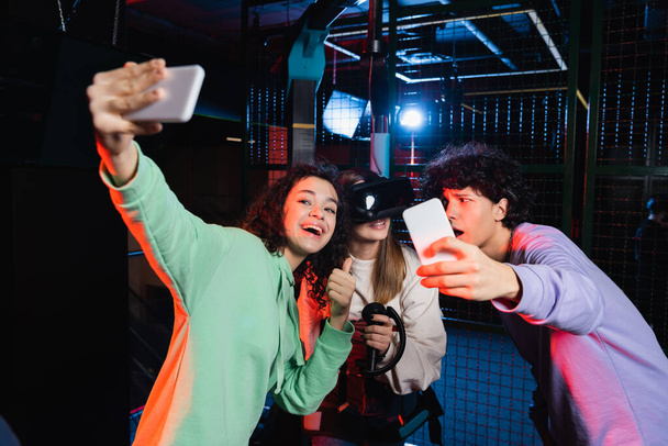 cheerful interracial teenagers taking selfie with friend in vr headset  - Zdjęcie, obraz