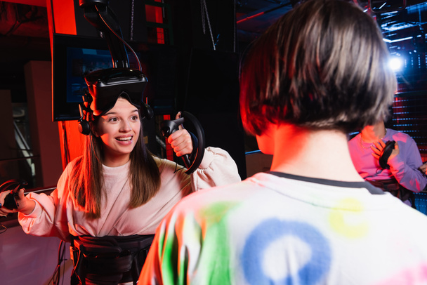 cheerful girl smiling near teenage boys in vr game zone, blurred foreground - Photo, Image