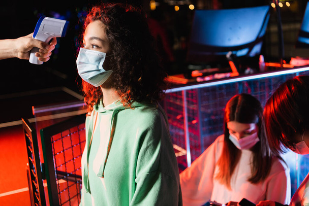ragazza afroamericana in maschera medica vicino controller con pirometro e amici adolescenti - Foto, immagini