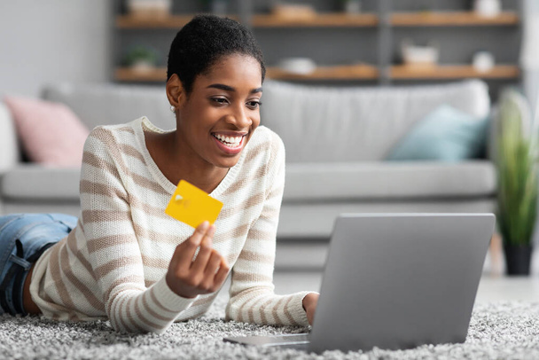 E-Commerce Concept. Gelukkig zwart vrouw met behulp van laptop en creditcard thuis - Foto, afbeelding