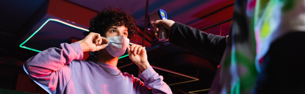 teenage gamer putting on medical mask near controller with pyrometer, banner - 写真・画像
