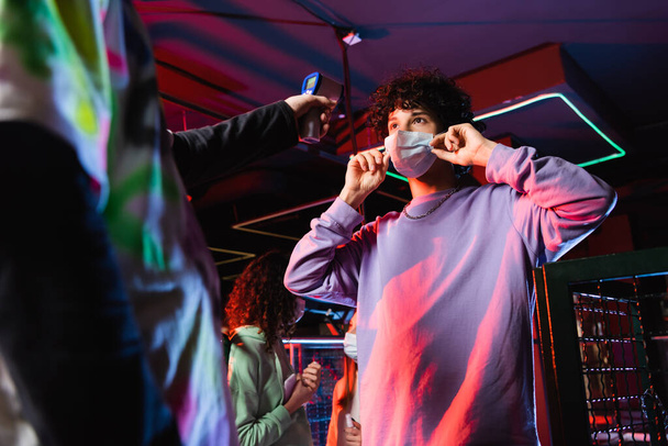 αγόρι που φοράει ιατρική μάσκα κοντά σε φίλους και θολή χειριστήριο με πυρόμετρο - Φωτογραφία, εικόνα