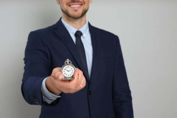 Happy businessman holding pocket watch on grey background, closeup. Time management - Photo, Image