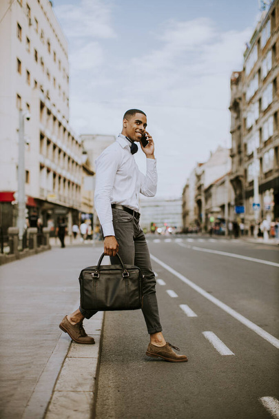 Jóképű, fiatal afro-amerikai üzletember mobiltelefont használ, miközben egy utcát vezet. - Fotó, kép
