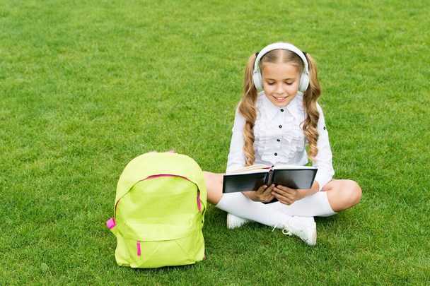 Language learning course. Girl child learn English sitting on green grass. Foreign language. Audio lesson - Valokuva, kuva