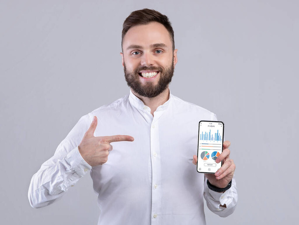 Ευτυχής επιχειρηματίας κρατώντας τηλέφωνο με analytics app στην οθόνη - Φωτογραφία, εικόνα