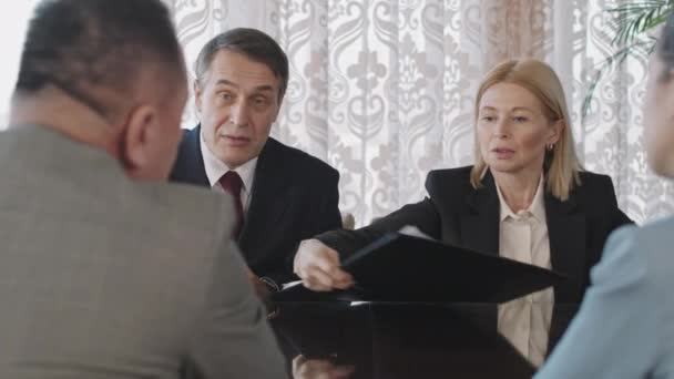 Waist-up PAN shot of four male and female business partners sitting at negotiation table discussing new successful project and signing contract - Materiał filmowy, wideo